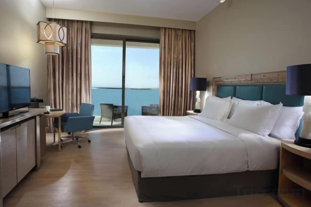 Een hotelkamer met een groot bed, een bureau met stoel, een televisie en uitzicht op de oceaan.