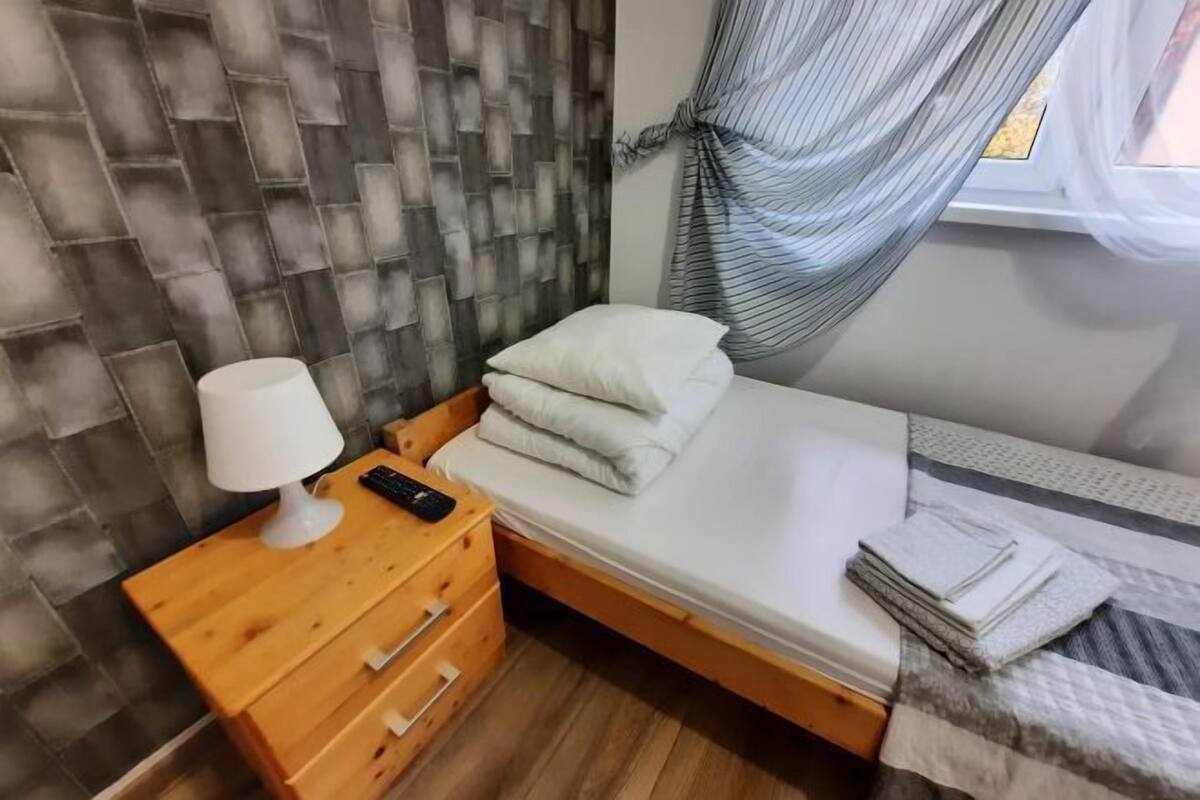 A single bed with a wooden headboard, a bedside table with a lamp, and a window with curtains.