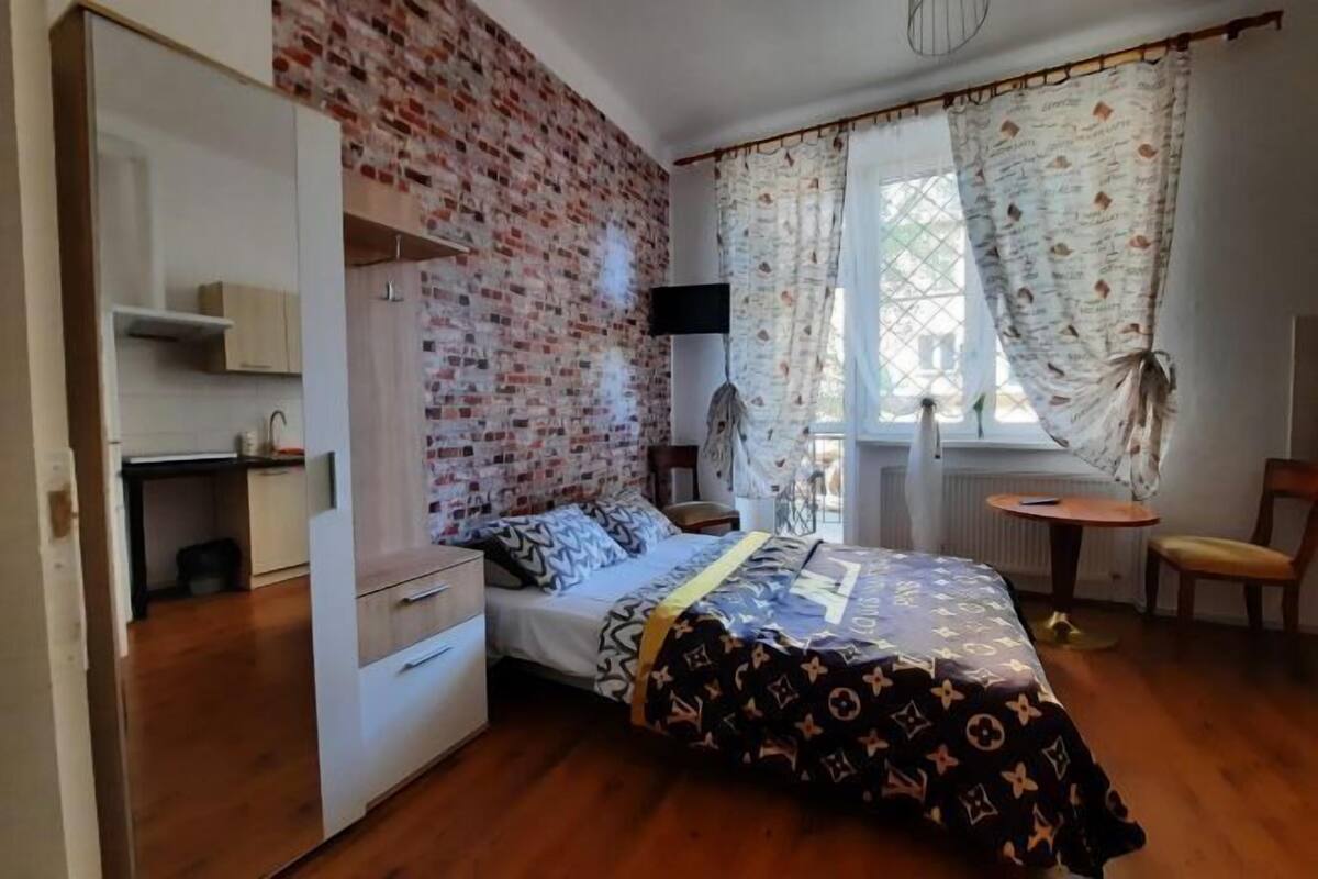 A bedroom with a bed, a wardrobe, a desk, a chair, and a window with curtains.