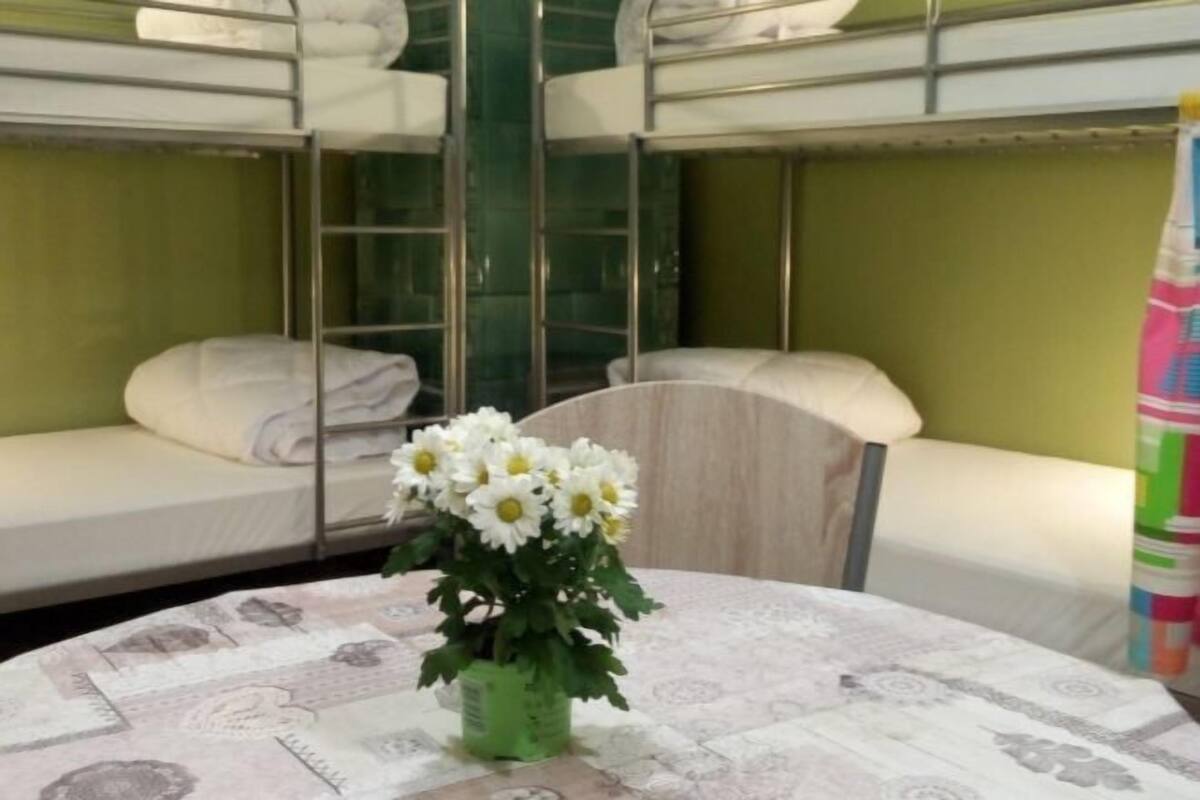 A hotel room with bunk beds, a round table with a patterned tablecloth, and a vase of white flowers.
