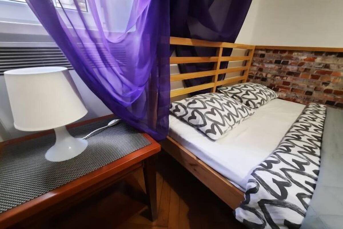 A bedroom with a wooden bed, patterned pillows, a white lamp, and a purple canopy.