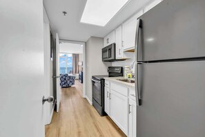 Un couloir étroit mène à une cuisine équipée d’un four à micro-ondes, d’un réfrigérateur et de placards.