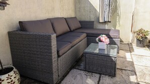 Um sofá de vime com almofadas, uma mesa de centro de vidro e um vaso com planta.