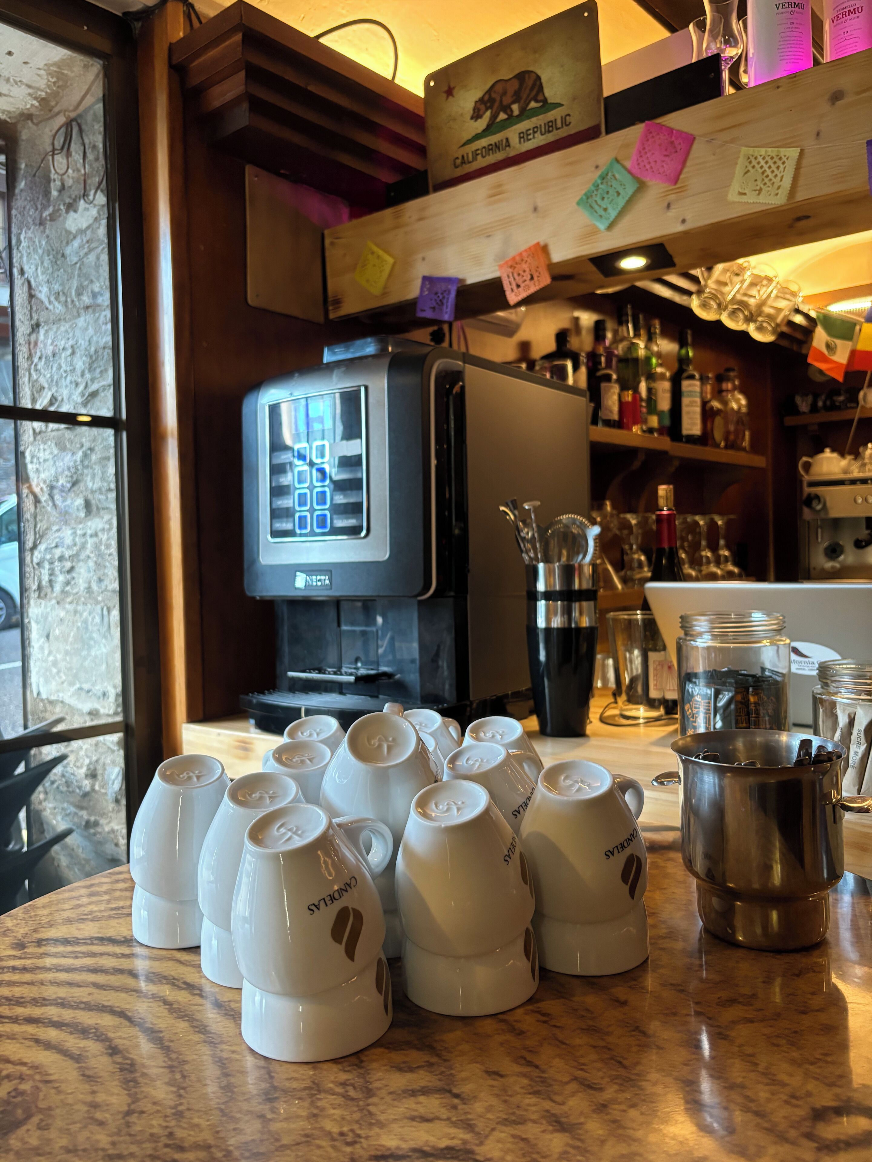 A coffee shop counter with a coffee machine, a variety of coffee cups, and a selection of beverages.