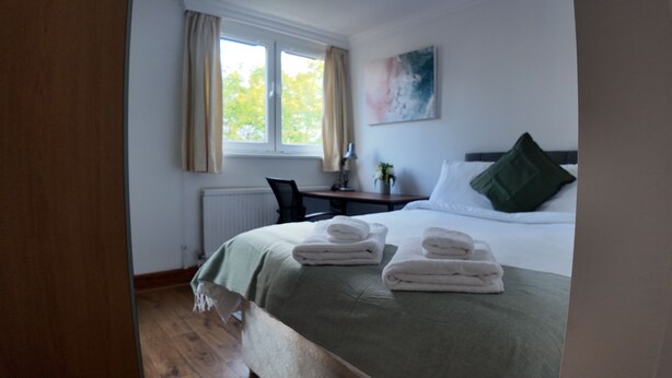 A hotel room with a bed, a desk, a chair, and a window with curtains.