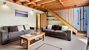 A cozy living room with two sofas, a coffee table, and a wooden staircase.
