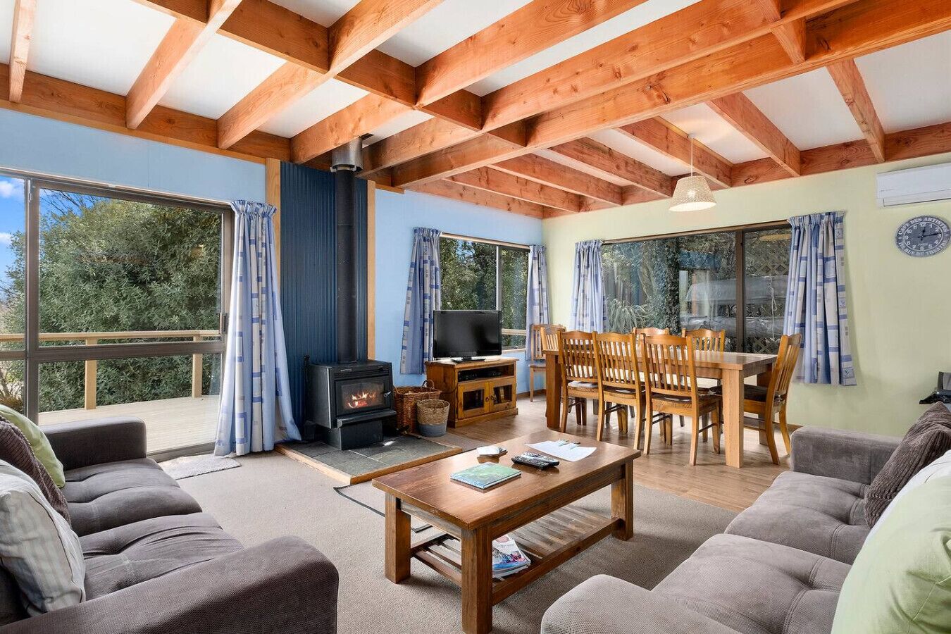 A cozy living room with a fireplace, wooden furniture, and large windows.