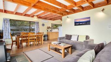 Un salón acogedor con una mesa de comedor de madera, un sofá gris y vistas al exterior a través de ventanas amplias.