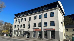 Un immeuble à plusieurs étages dont le rez-de-chaussée est occupé par des locaux commerciaux, notamment un magasin dont la devanture est bien visible et porte une enseigne.