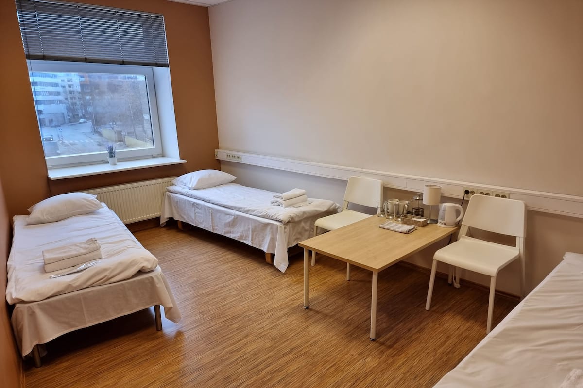 Een kamer met twee eenpersoonsbedden, een kleine tafel met stoelen, een radiator en een raam met zonwering.