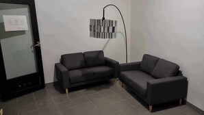 Une pièce avec deux canapés sombres, un lampadaire et une porte dotée d’un panneau en verre.