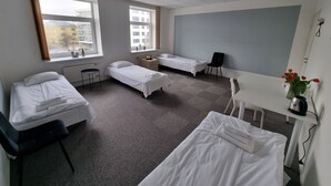 Une chambre d’hôtel avec deux lits simples, un bureau, une chaise et une fenêtre donnant sur des immeubles.