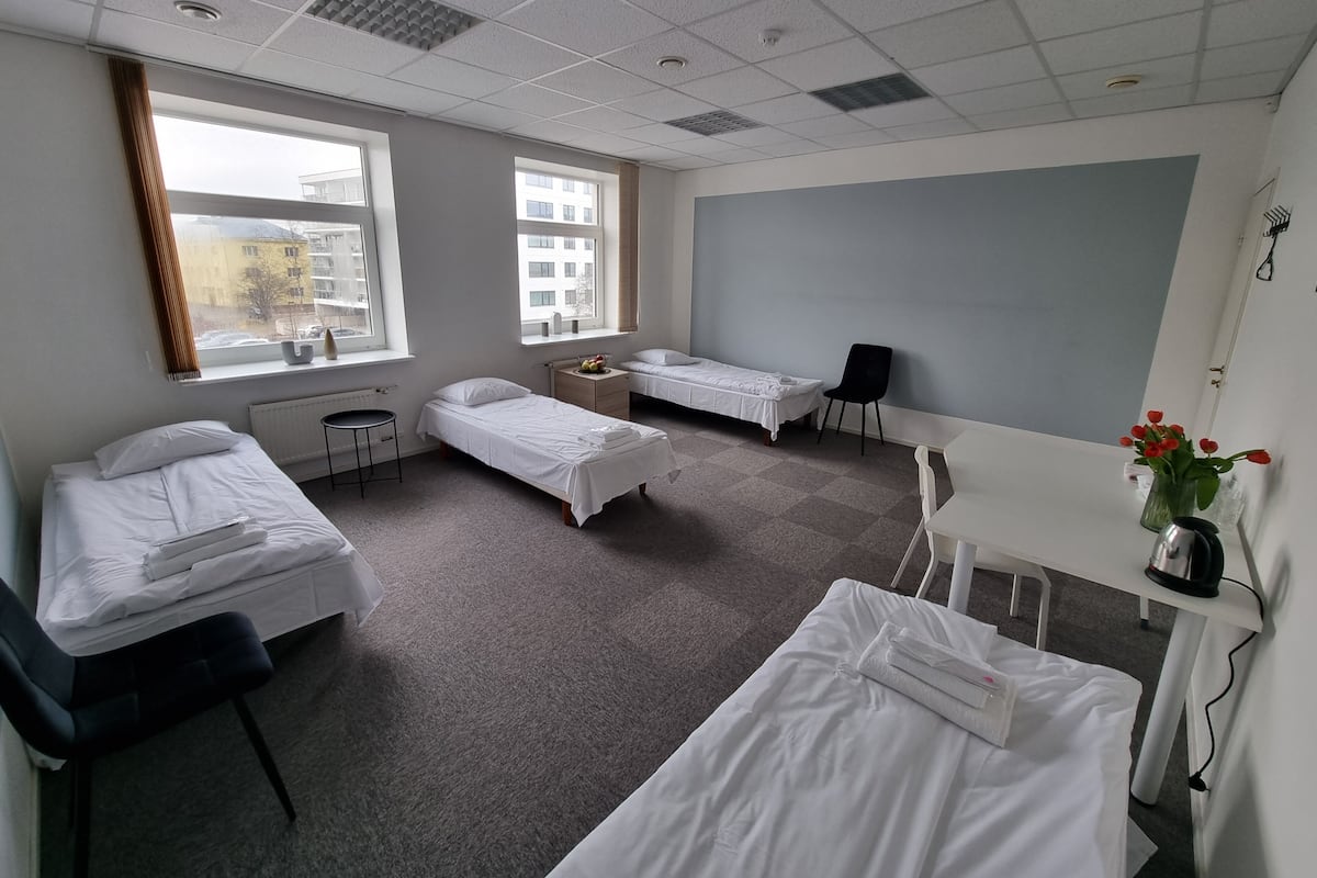 Een hotelkamer met twee enkele bedden, een bureau, een stoel en een raam met uitzicht op gebouwen.