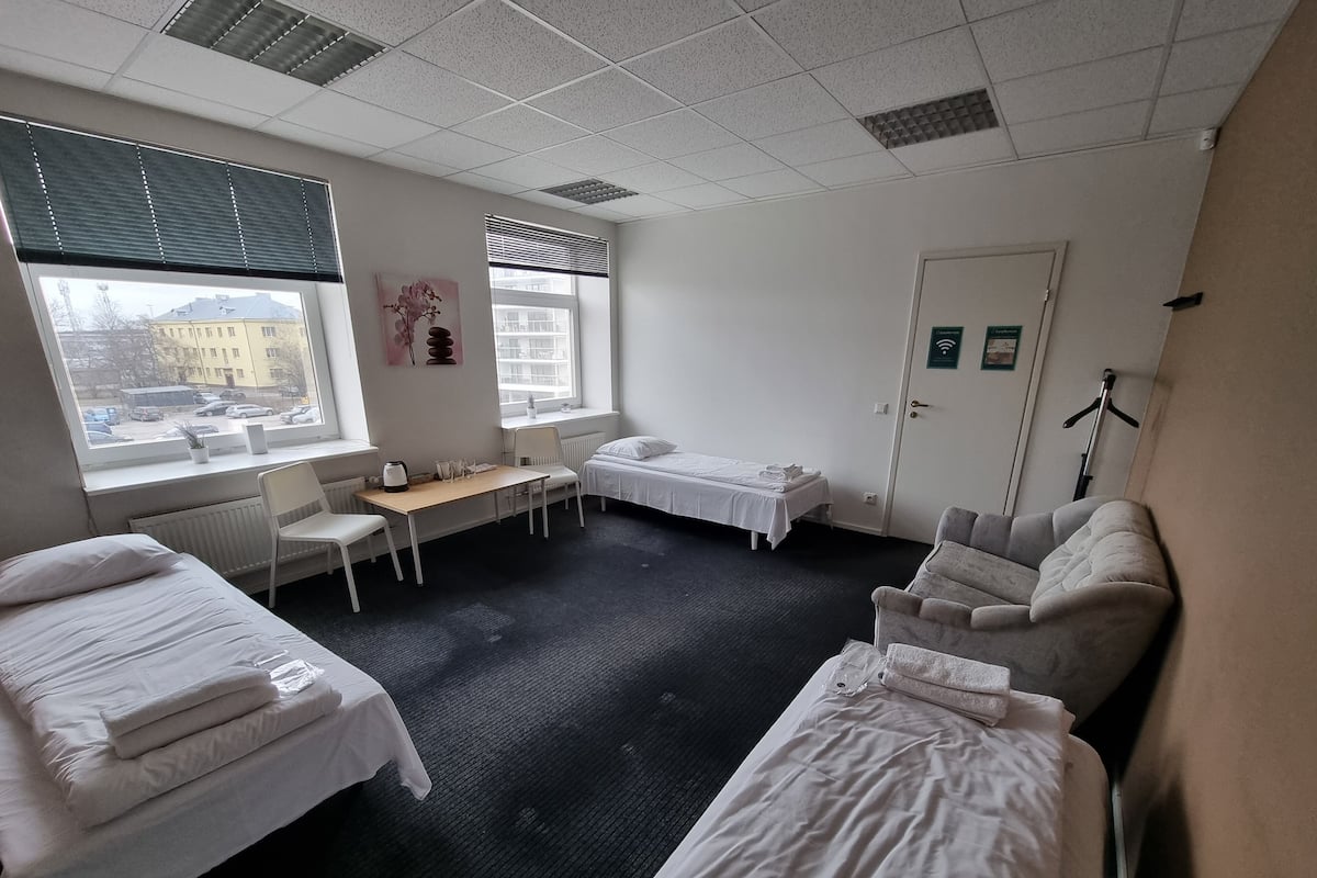Een hotelkamer met twee éénpersoonsbedden, een klein bureau, een stoel, een raam met zonwering en een radiator.