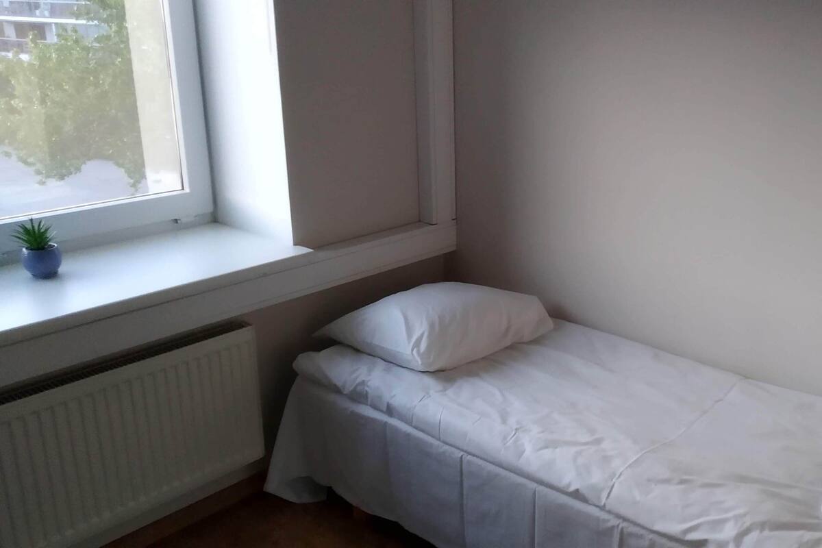 Een kleine kamer met een enkel bed, een raam, een radiator en een bloempot op de vensterbank.