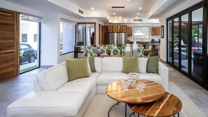 A modern living room with a white sectional sofa, a wooden coffee table, and a view of the kitchen and outdoor patio. - Casa Rio Mar Luxury Villas: The Ultimate Double Escape! 2 Luxury Villas 14 BR/BA (Jaco)