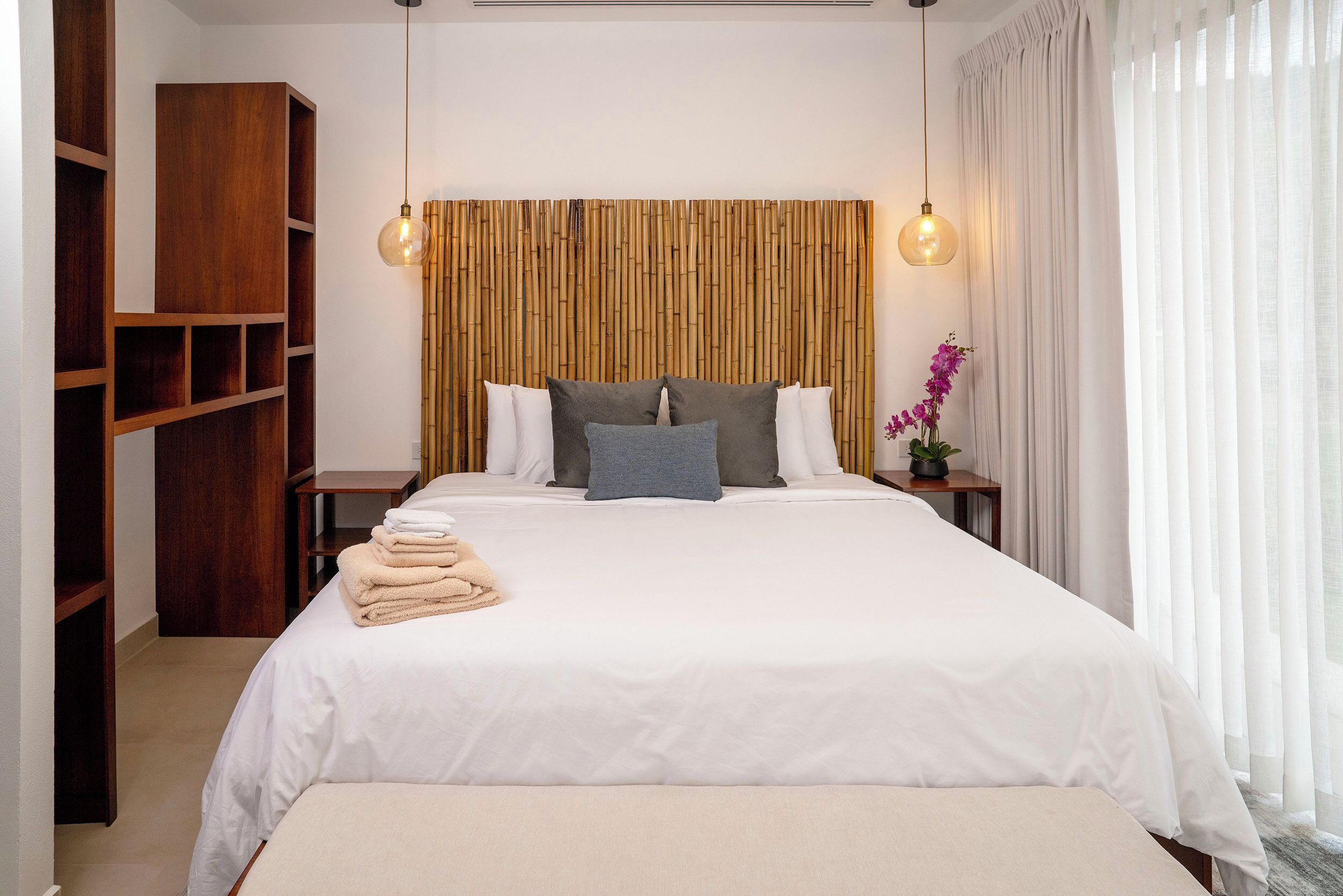 Una cama bien hecha con sábanas blancas, un cabecero de madera y dos lámparas de noche.