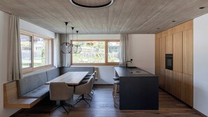 A modern kitchen with a wooden ceiling, built-in wooden cabinets, a central island, and a dining area with a bench and chairs. - Haus Jolanda by we rent (Piesendorf)