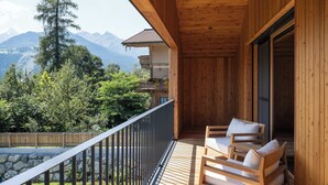 A wooden balcony with a view of mountains, a stone wall, and two wooden chairs. - Haus Jolanda by we rent (Piesendorf)