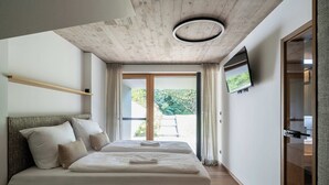 A modern bedroom with a large bed, a TV mounted on the wall, and a sliding glass door leading to a balcony. - Haus Jolanda by we rent (Piesendorf)