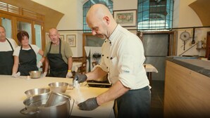 Un chef prépare des plats dans une cuisine dotée de meubles en bois et d’une grande fenêtre.