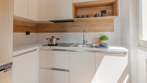 Une cuisine moderne avec des meubles blancs, un plan de travail en bois, une étagère intégrée où sont posées des tasses et une petite plante.
