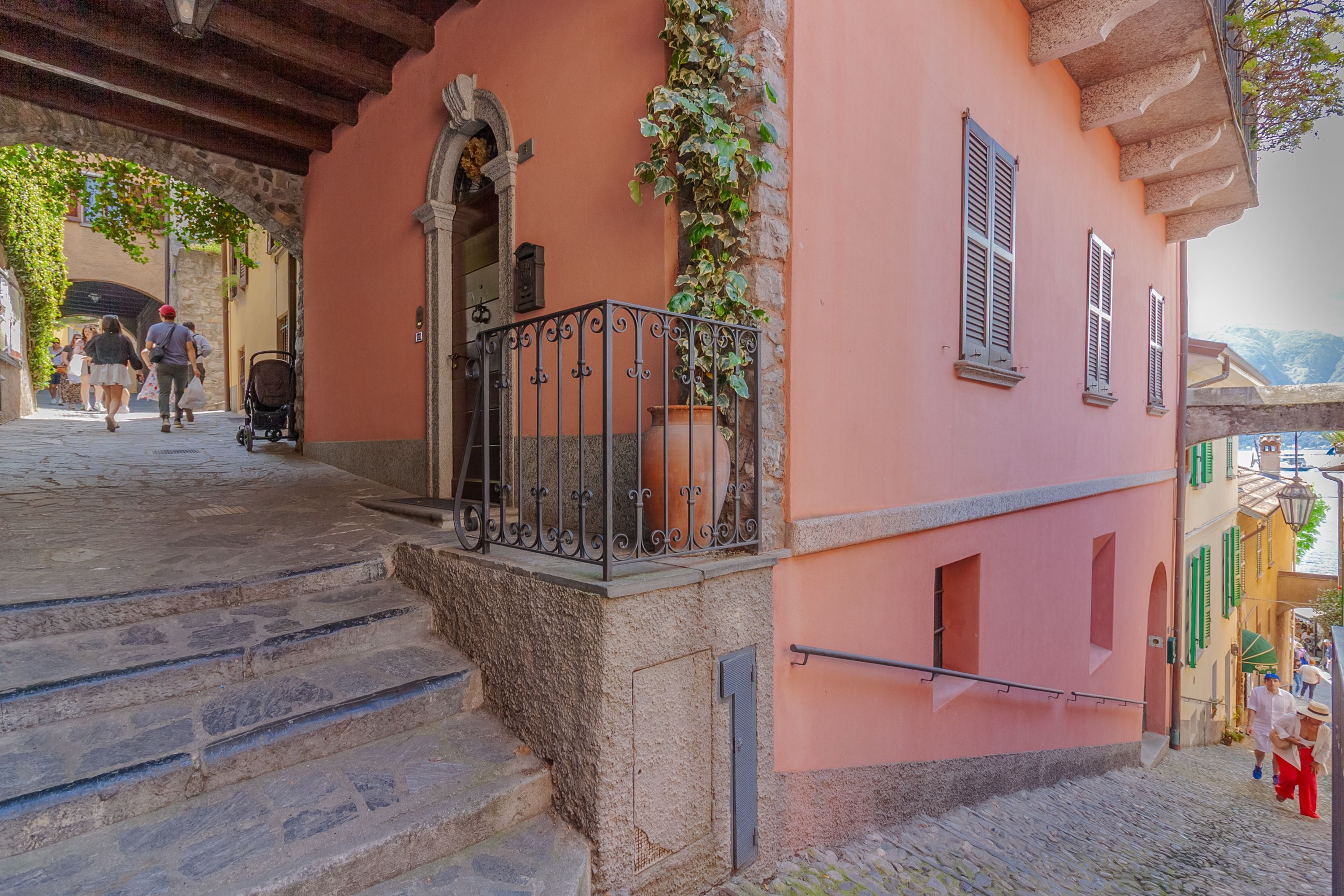 A stone staircase leading to a pink building with a wrought iron balcony and a potted plant.