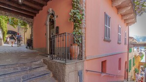 Un escalier en pierre mène à un bâtiment rose doté d’un balcon en fer forgé et d’un pot de fleurs.