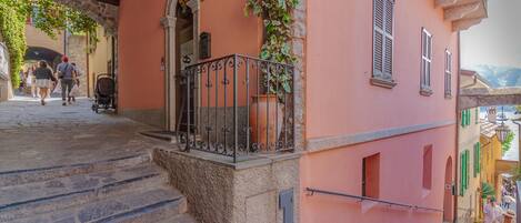 A stone staircase leading to a pink building with a wrought iron balcony and a potted plant.