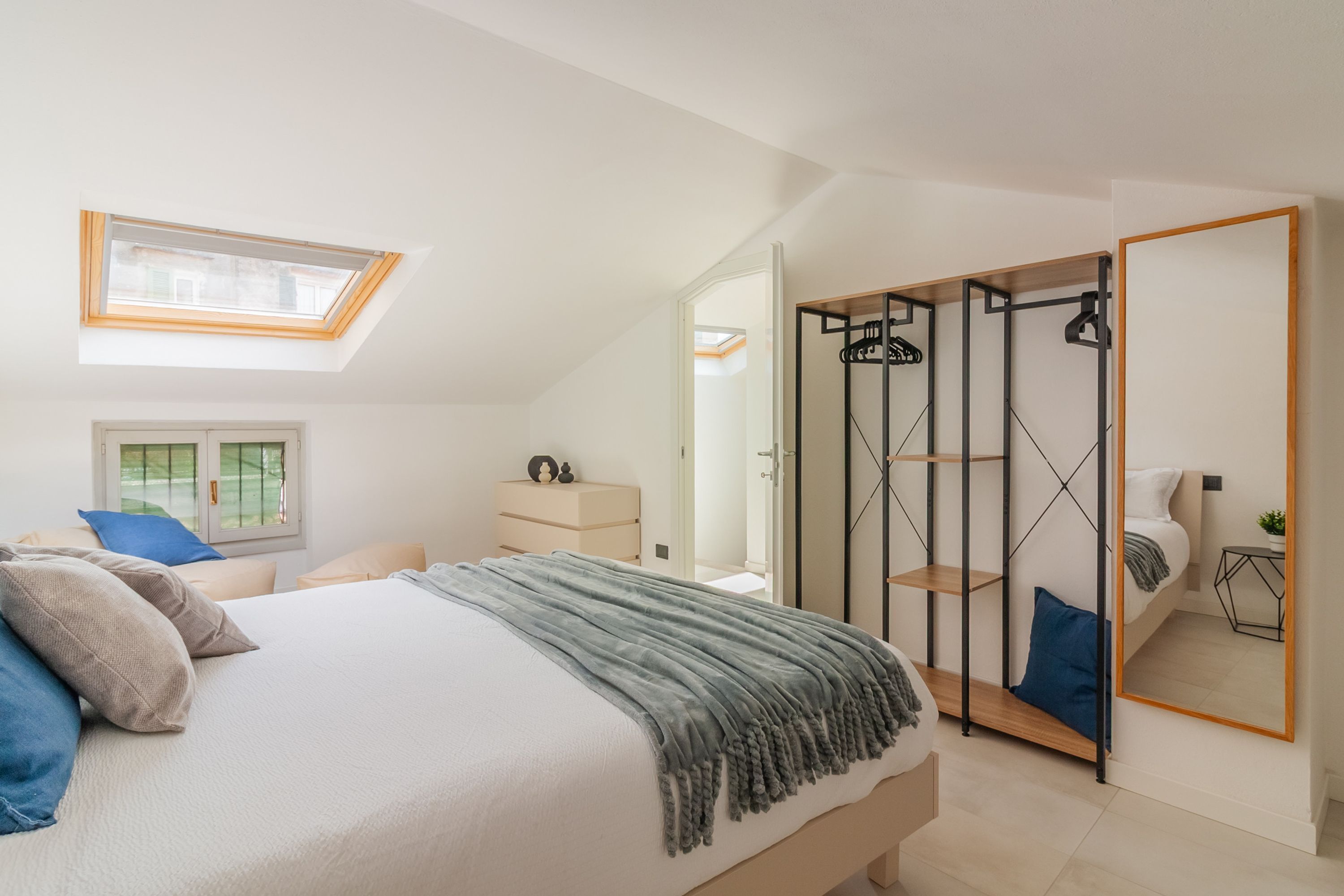 Un dormitorio con cama, tragaluz, armario y espejo.