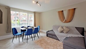 Un salon moderne avec un canapé gris, des fauteuils bleus, une table à manger et une grande fenêtre avec des rideaux.