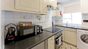 Une cuisine avec des meubles blancs, un four à micro-ondes, un grille-pain, une bouilloire et un lave-linge.