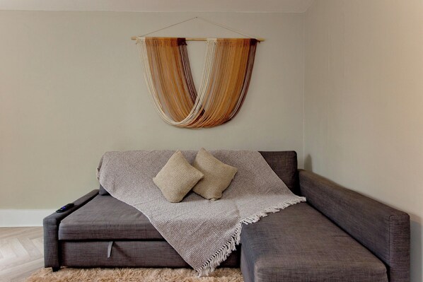 A modern living room with a grey sofa, a woven hanging decoration, and a textured throw blanket.