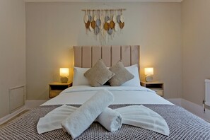 A neatly made bed with a patterned bedspread, two pillows, and rolled towels. - Imperial Leinster Garden Apartment (London)