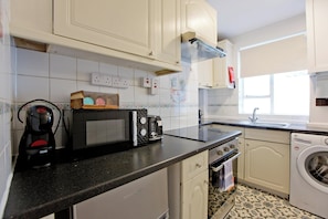 Una cocina con armarios blancos, encimera negra, cafetera, tostadora, microondas, fregadero y lavadora.