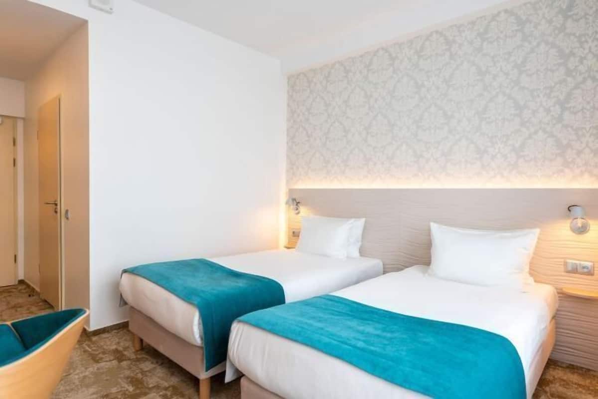 Habitación de hotel con dos camas, un papel tapiz estampado y una mesita de noche con lámpara.