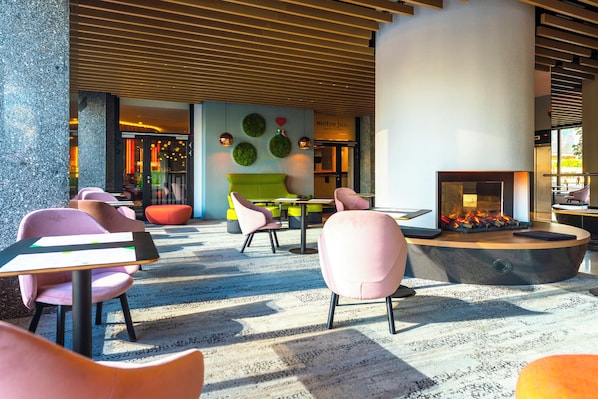 A modern lounge area with seating, a fireplace, and a wall with circular green decorations. - Metropol (Warsaw)