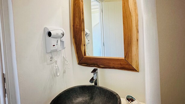 A bathroom with a round stone sink, a wooden-framed mirror, and a white wall. - Divers house in Mykonos (Mykonos)