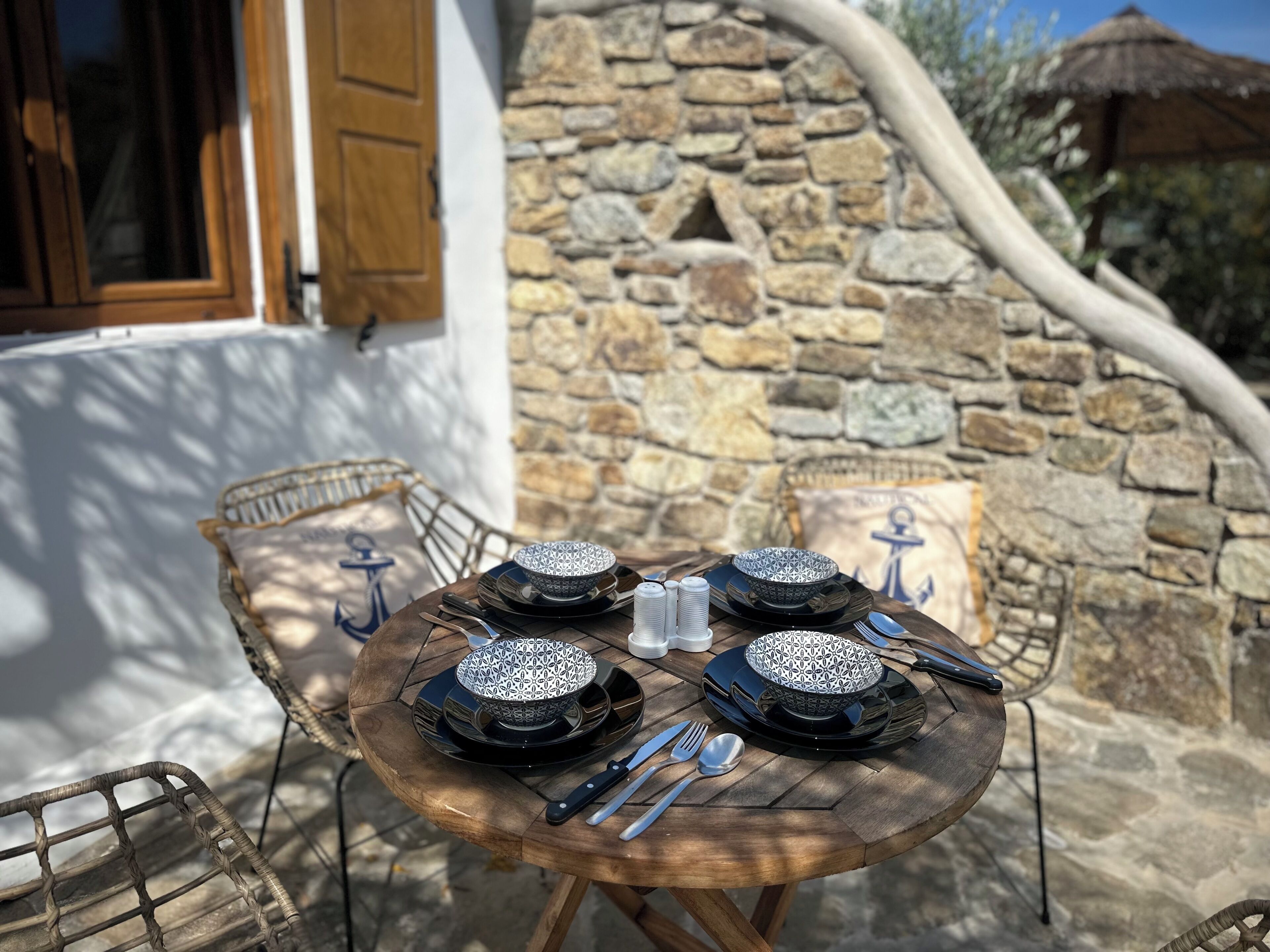 A round wooden table set with four patterned bowls, silverware, and salt and pepper shakers.