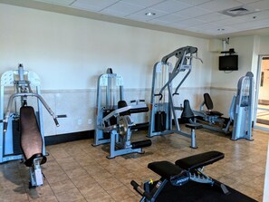 Une salle de sport équipée de divers appareils d’exercice, d’un banc et d’un téléviseur fixé au mur.