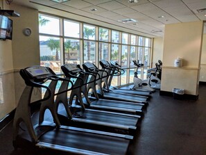 A row of treadmills in a room with large windows overlooking a pool area. - Crystal Towers 609, Corner Unit Your Perfect Beach Getaway Awaits You! (Gulf Shores)