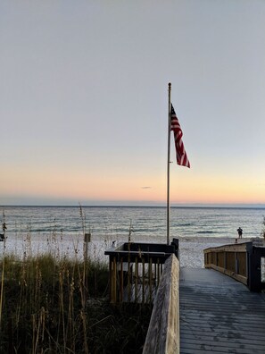 A wooden boardwalk leading to a beach with an American flag on a flagpole.