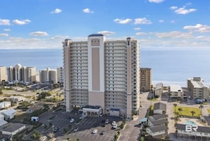 Um hotel moderno com uma torre central, estacionamento e vista para o oceano.
