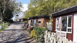Een rij houten stacaravans met een onverhard pad erdoorheen, omringd door bomen en een houten hek.