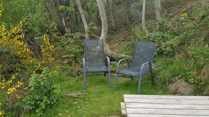 Twee metalen stoelen en een houten tafel in een natuurlijke omgeving, met gras en gele bloemen.