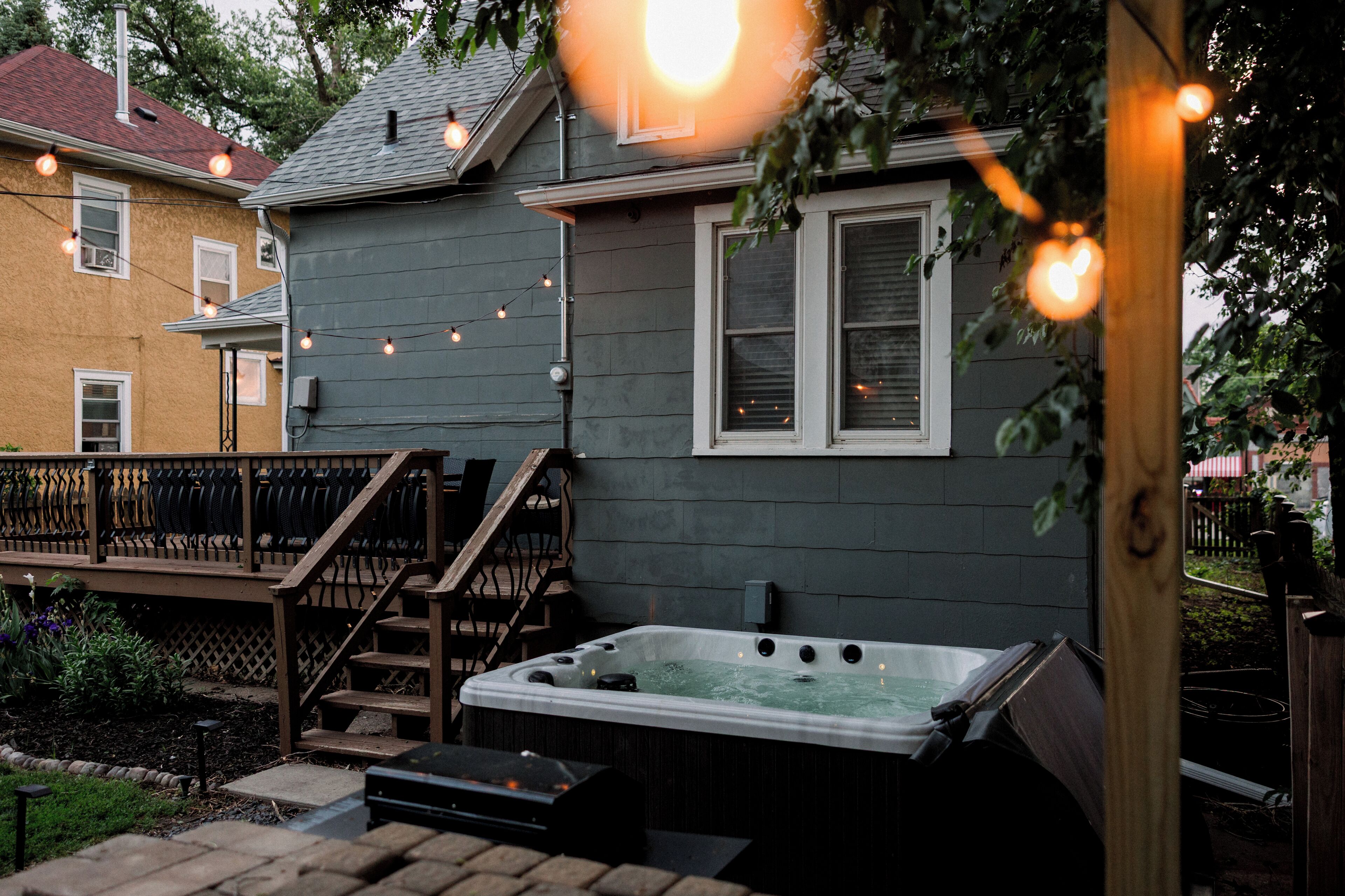A backyard with a hot tub, wooden deck, and string lights.