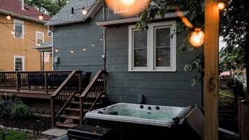 A backyard with a hot tub, wooden deck, and string lights.