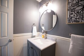 A bathroom with a white vanity, a round mirror, and a light fixture above the mirror.