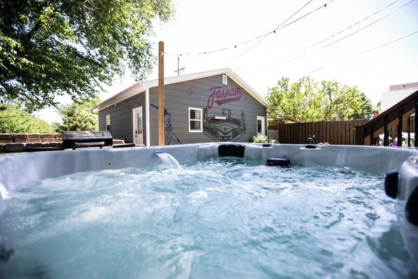 A hot tub with a wooden deck and a house with a mural in the background.