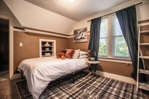 A bedroom with a bed, a nightstand, a window with curtains, a wall-mounted shelf, and a painting.